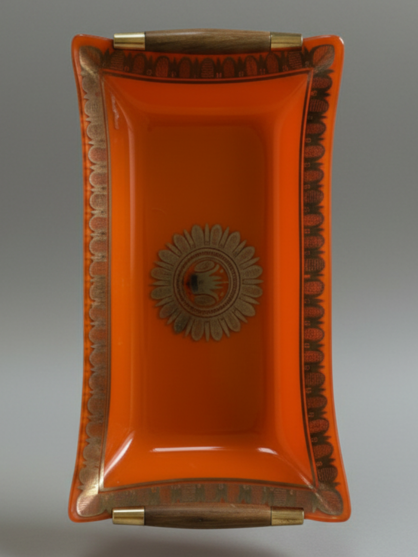 Georges Briard orange glass serving tray showing gilt border, curved form and dark wood handles.