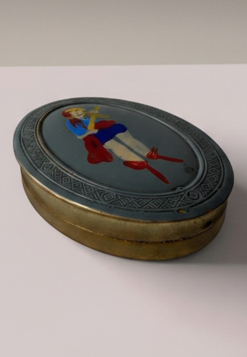 Atlas & Arden 1930s oval brass compact with hand-painted British folk figure, blue dress, red boots, and geometric border.