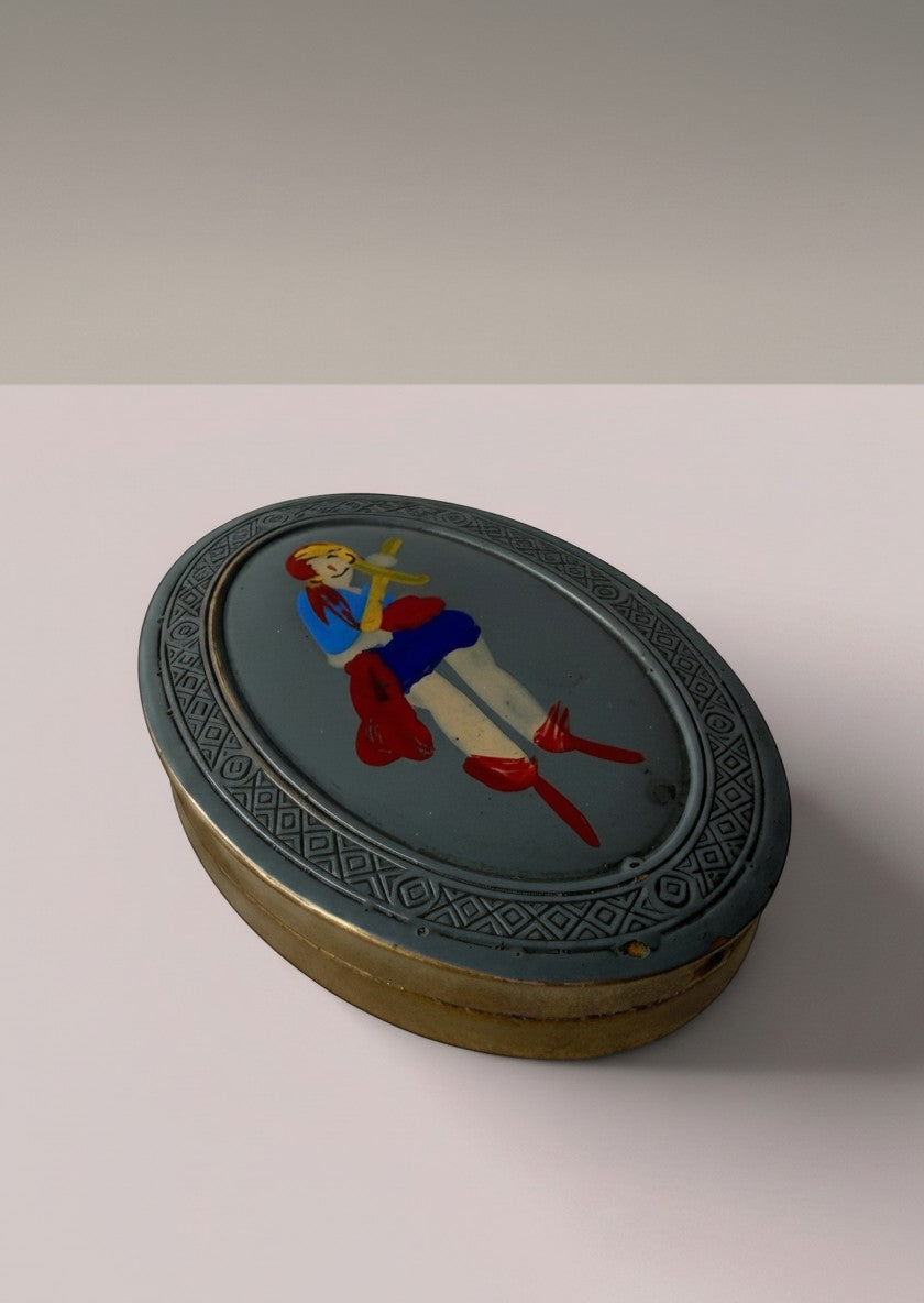 Atlas & Arden 1930s oval brass compact with hand-painted British folk figure, blue dress, red boots, and geometric border.