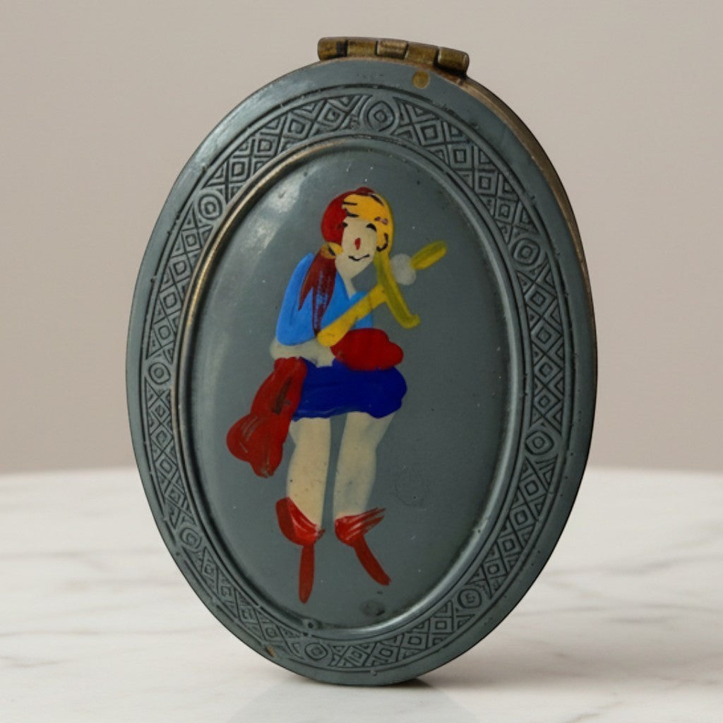 Atlas & Arden 1930s oval brass compact with hand-painted British folk figure, blue dress, red boots, and geometric border.